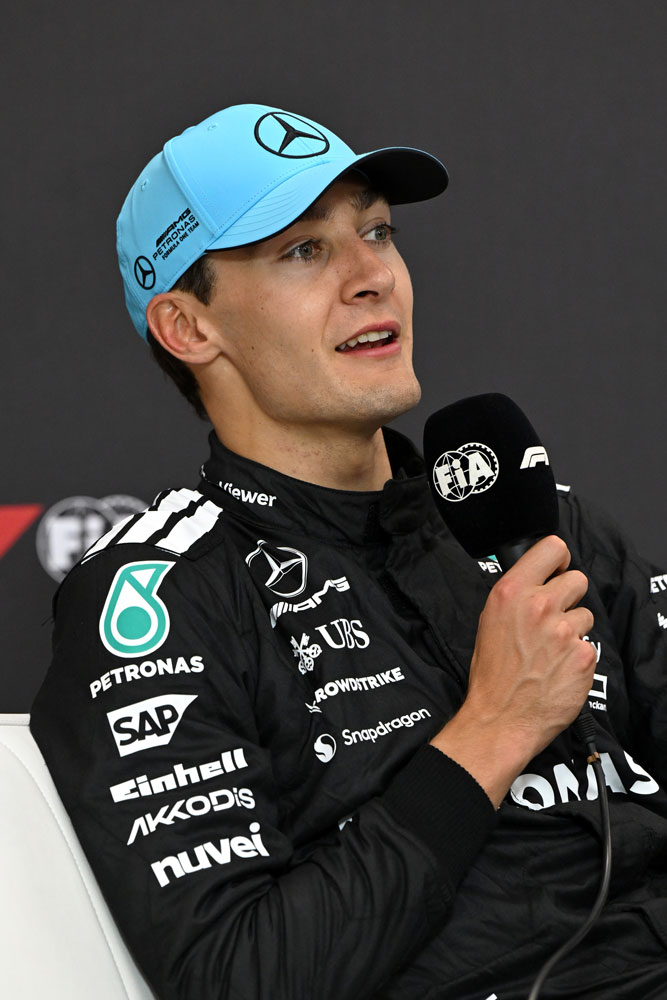 Formula 1 driver George Russell with a microphone in his right hand.