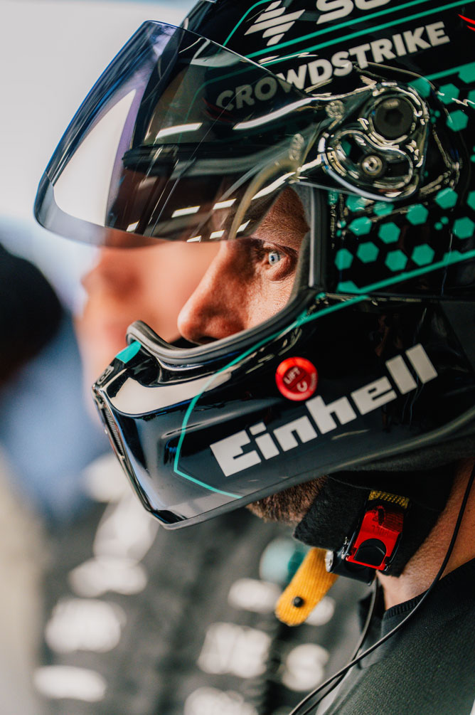 A Formula 1 crew member is wearing a helmet and looking to the side with focus.